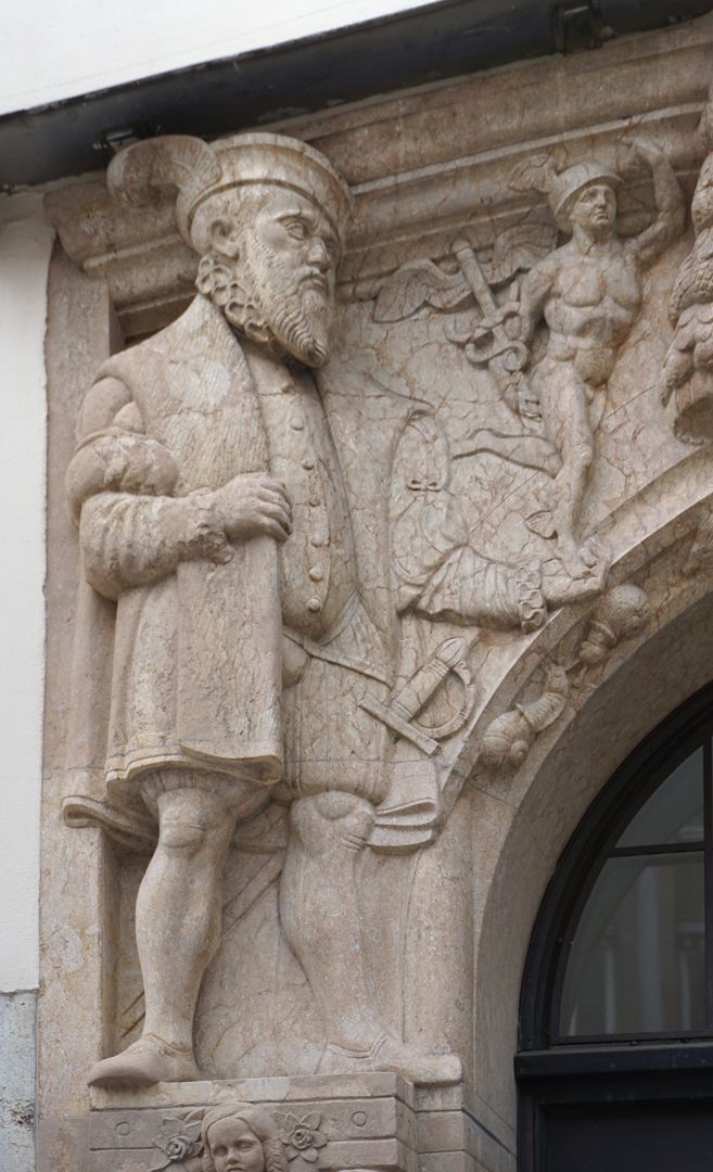 Portal linke obere Ecke: ein Bürger in Renaissancekleidung trägt Merkur (römischer Schutzgott der Händler) in seiner linken Hand
