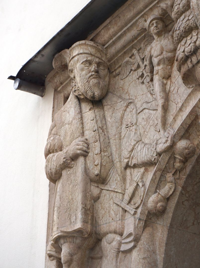 Portal linke obere Ecke: ein Bürger in Renaissancekleidung trägt Merkur (römischer Schutzgott der Händler) in seiner linken Hand / Schrägansicht