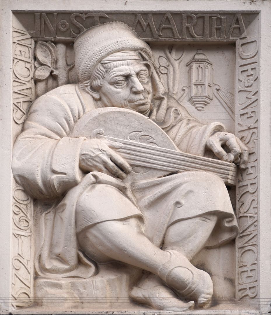 Pfarrhaus von St. Martha Lautenspieler, sein Instrument stimmend von Max Heilmaier (1909) mit Inschrift, die an die Meistersinger erinnert, welche 1572-1620 in der Kirche St. Martha sangen