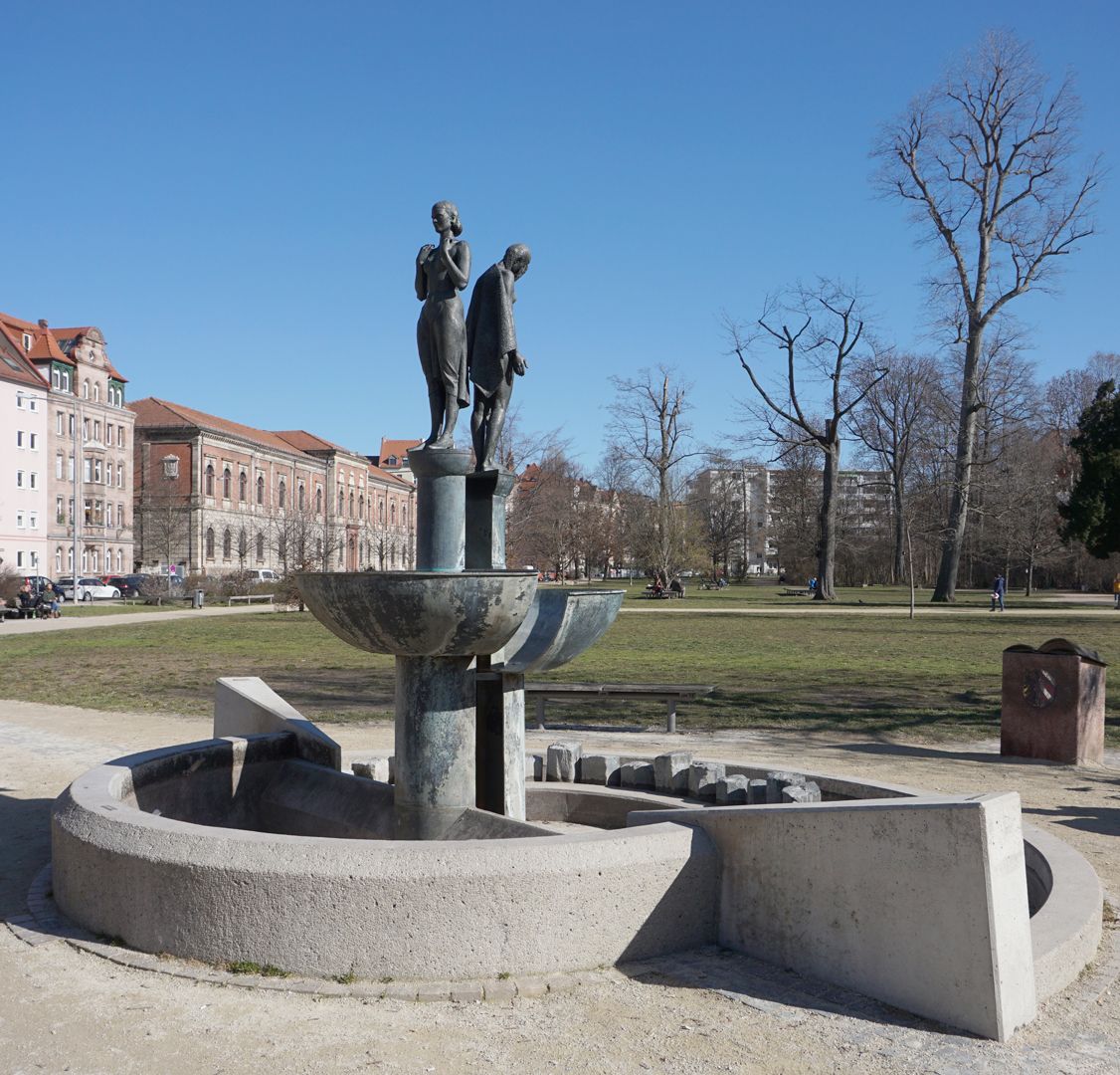 Norisbrunnen Zweigeteilte Brunnenanlage. Obere Brunnenschale mit aufrecht stehender Frauengestalt. Untere offene Brunnenschale mit gebeugter entblößter Frauengestalt.